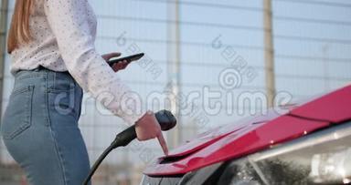 女人在充电器插入她的现代新红色电动车插座。 女士正在为电动车充电